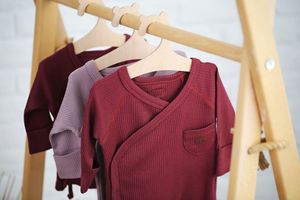 Baby clothes in burgundy and mauve tones hanging on a wooden rack.