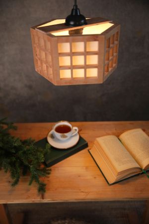 Cozy reading nook with hexagonal pendant lamp illuminating open book and tea cup on wooden table.
