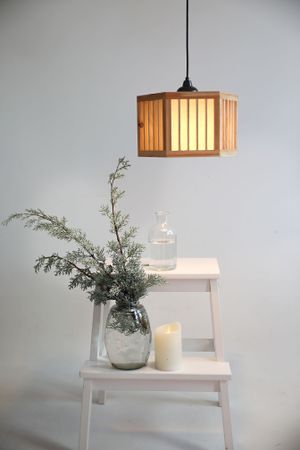 Modern wooden pendant lamp hanging above white ladder shelf with greenery and candle decor.