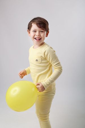 A joyful child in yellow pajamas playing with a yellow balloon against a gray background.