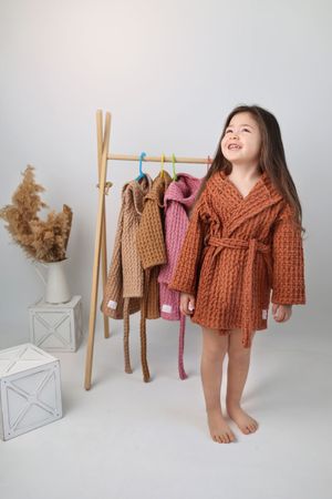 Cozy knit bathrobes displayed on wooden clothing rack with decorative pampas grass and geometric decor.