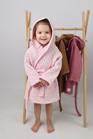 Pink quilted bathrobe displayed against minimalist clothing rack with other robes hanging.