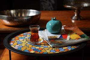 A traditional Turkish tea set on a colorful mosaic tray with a turquoise teapot and glass cup.