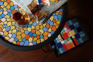 Colorful mosaic glass table top with geometric patterns in orange, blue and gold tones beside patterned coasters.
