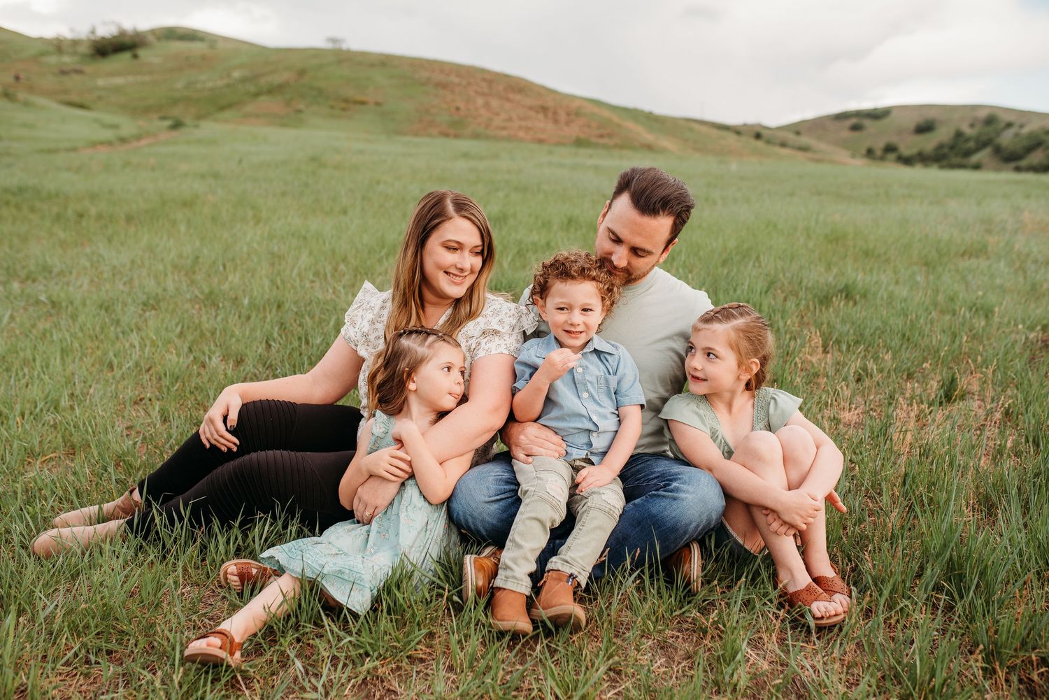 A family sitting together on grassy hillside during outdoor portrait session.
