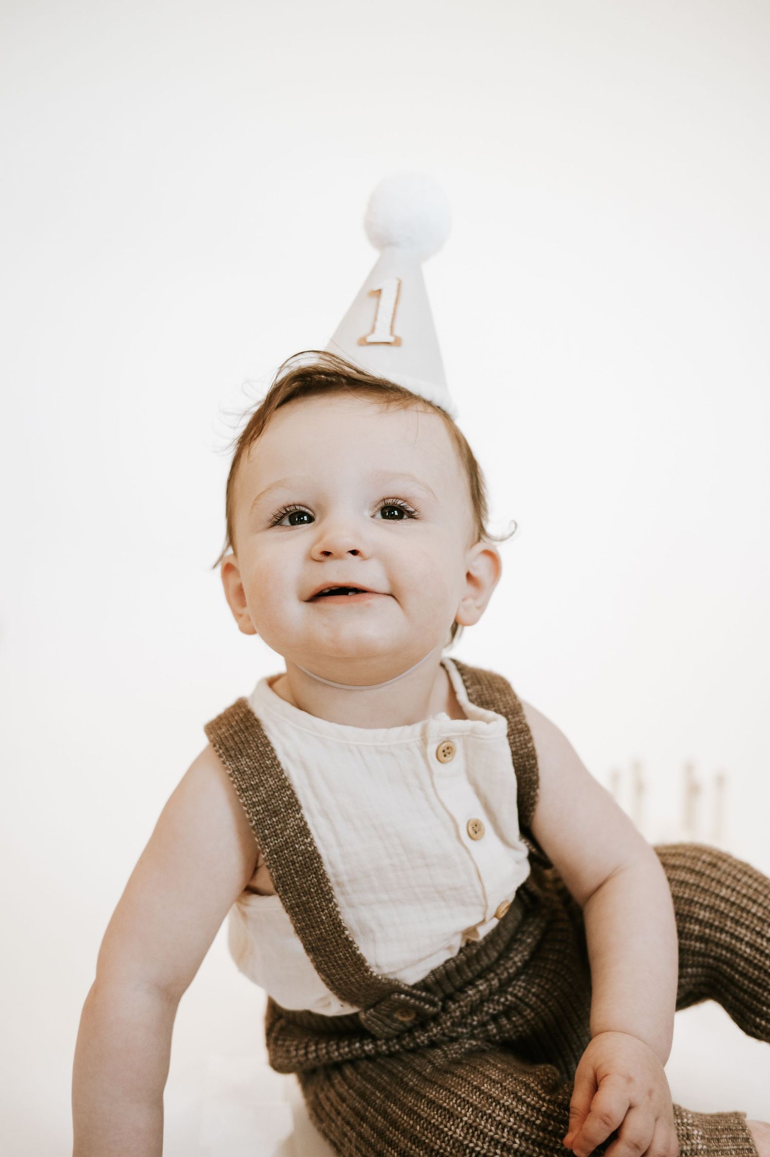 Sweet first birthday portrait with baby wearing white party hat with gold number one.