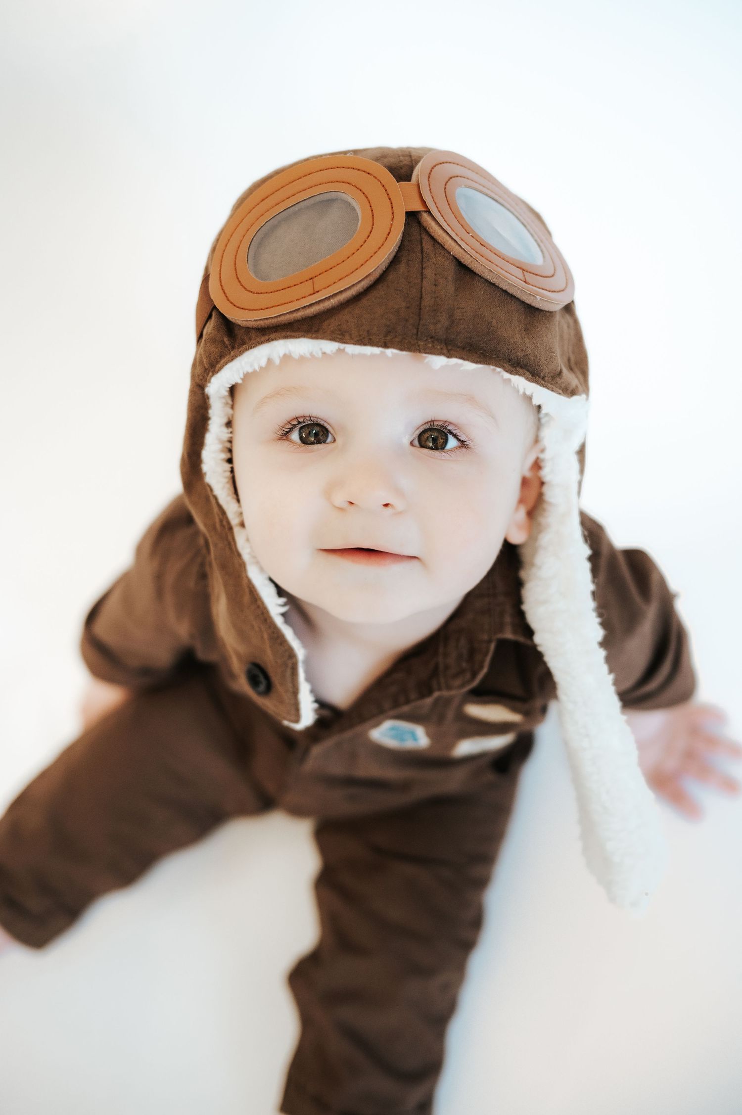 Little one wearing vintage aviator costume with brown leather cap and goggles against white background.