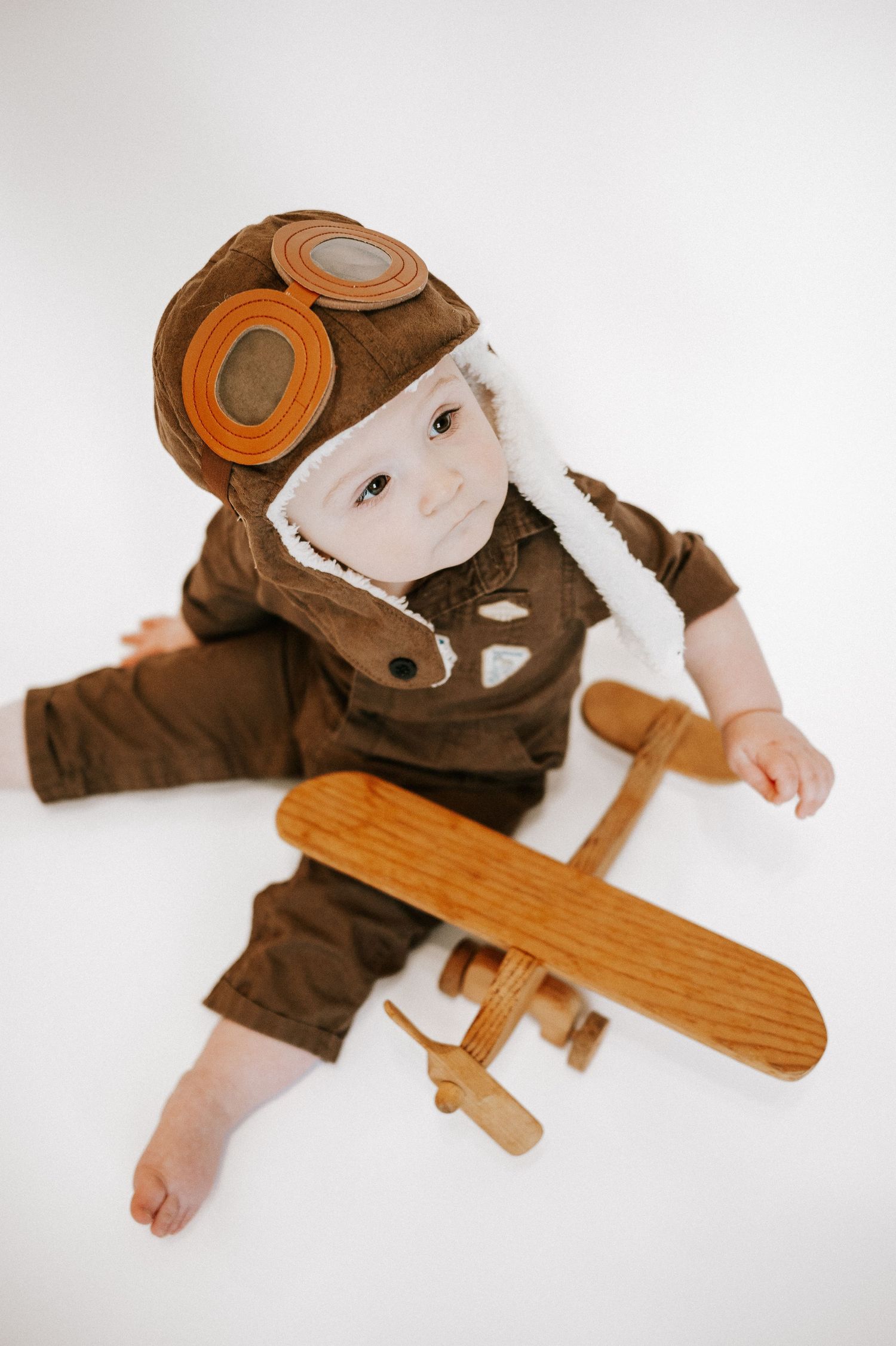 Overhead view of baby in vintage pilot costume playing with wooden toy airplane.