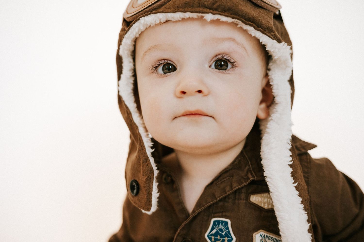 Close up portrait of toddler in brown aviator hat with fuzzy white trim.