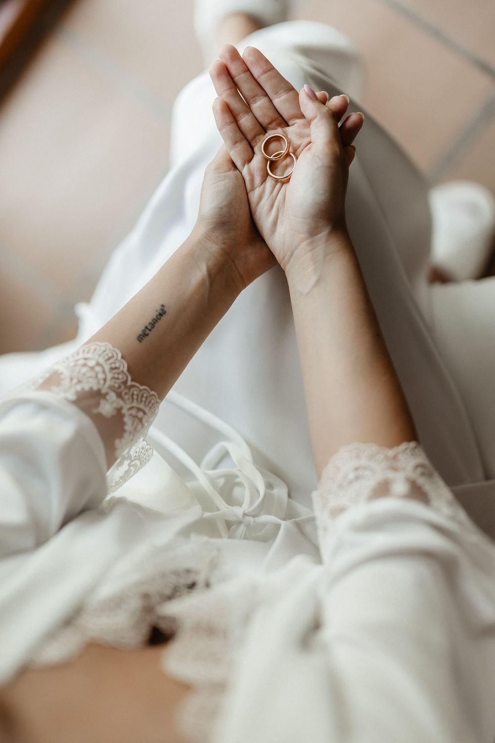 Close-up of hands with lace sleeves and wedding rings intertwined in romantic poses against soft white fabric.