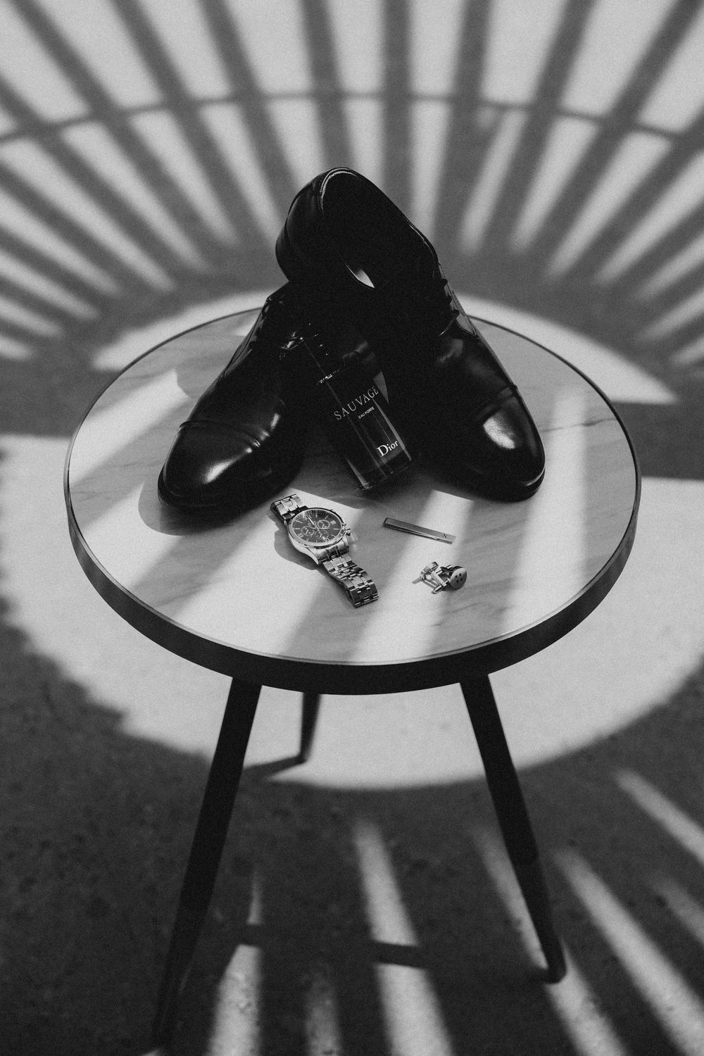 Black shoes on a white circular table cast dramatic radiating shadows in a striking monochromatic composition.