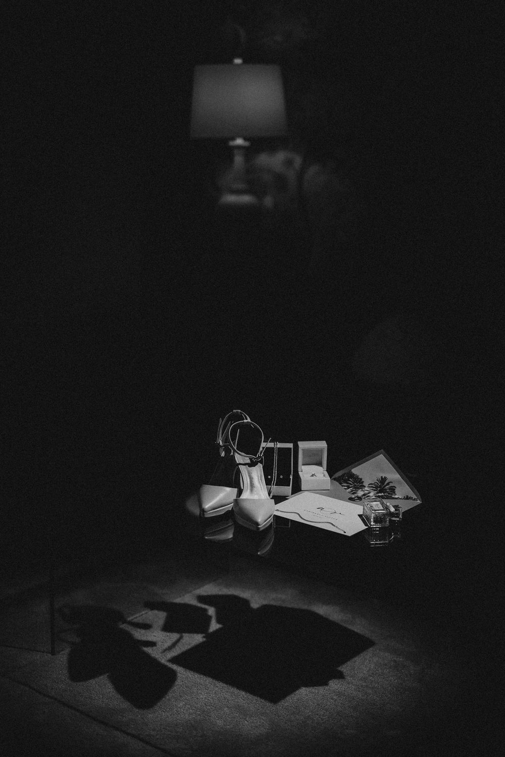 Dramatic black and white still life of desk items casting long shadows under lamplight at night.