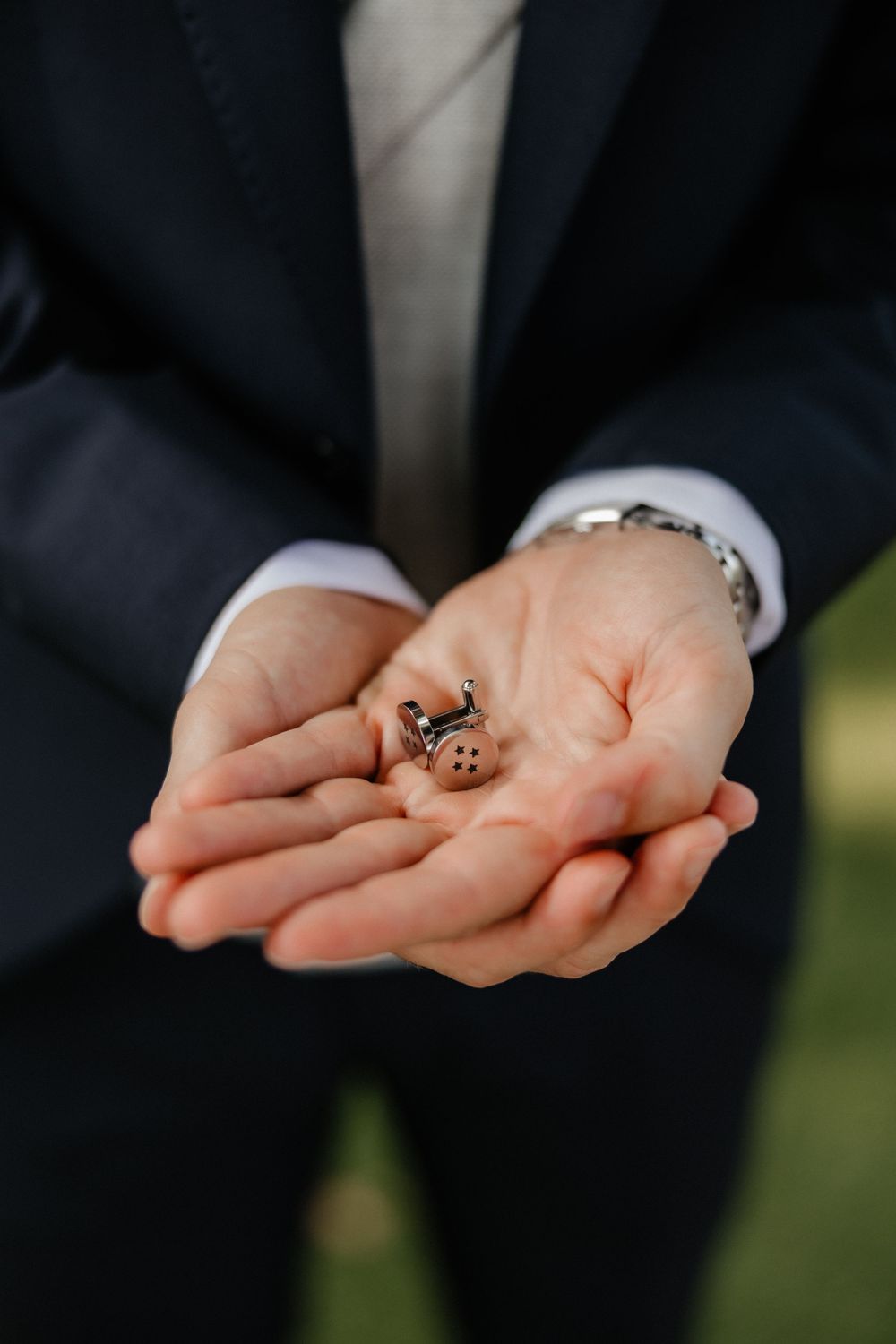 A sequence of hands in black suit sleeves holding and displaying a small wedding ring against a dark background.