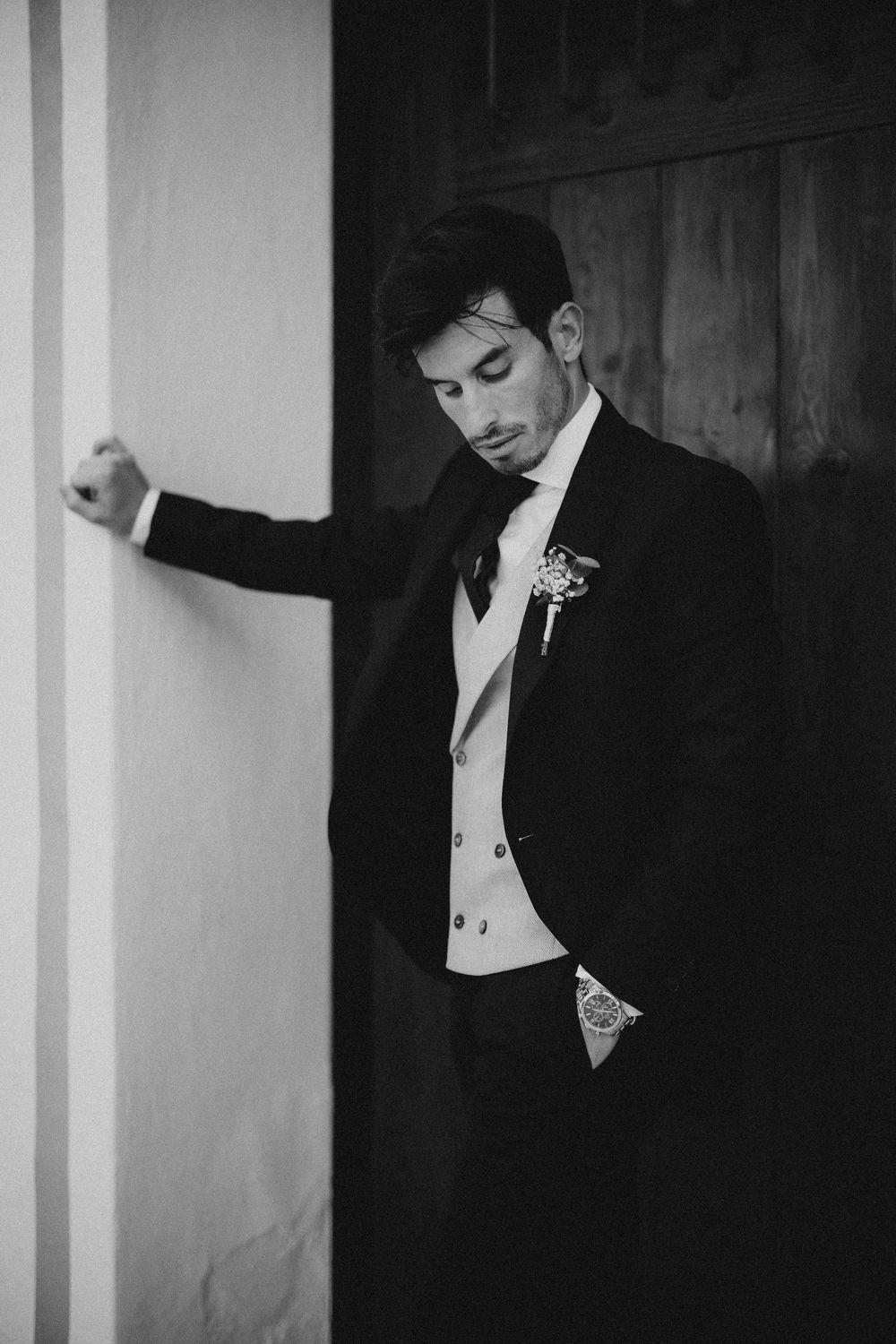 Black and white artistic portrait showing a figure in formal attire against a stark architectural backdrop with columns.