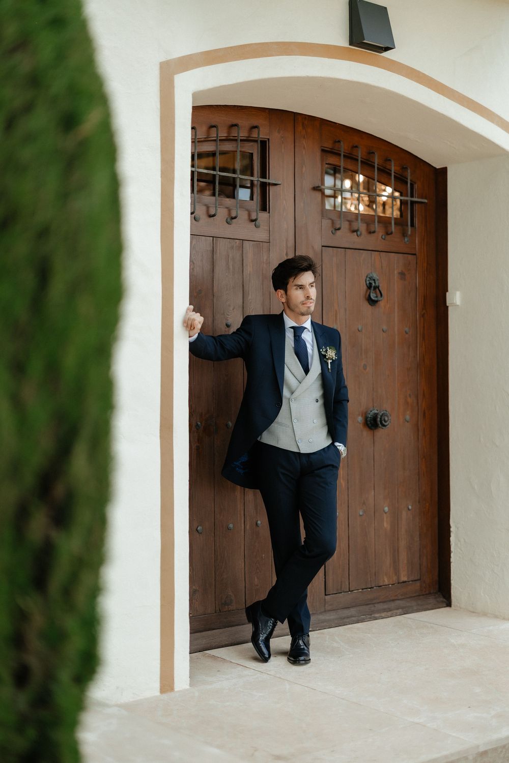 A person in a formal black tuxedo and bowtie poses stylishly against a wooden arched door in multiple shots.