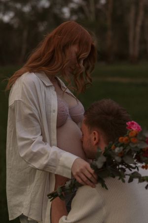 An intimate maternity moment with flowers in a dreamy outdoor setting.