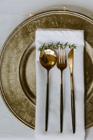 Gold forks and utensils arranged on white napkins against metallic charger plates in a progressive sequence.
