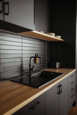 Modern black kitchen cabinets with wooden countertops and minimalist hardware in dramatic lighting.