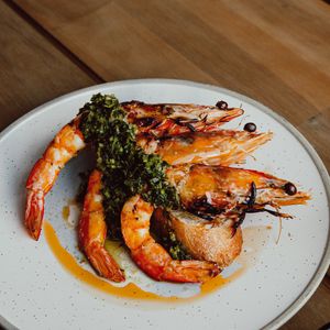 Grilled prawns with broccoli and sauce plated elegantly on white ceramic dishes.