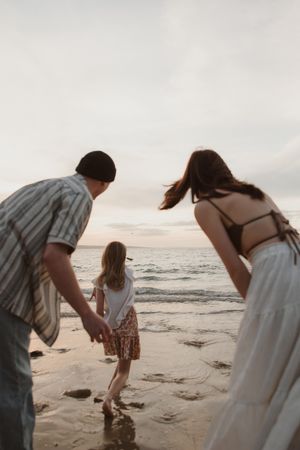 A family holds hands while walking together on a beach at sunset.