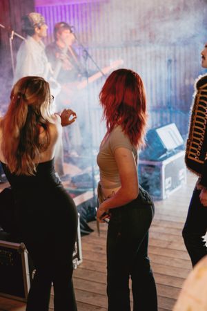 People dancing at a concert with purple lighting and atmospheric smoke effects.