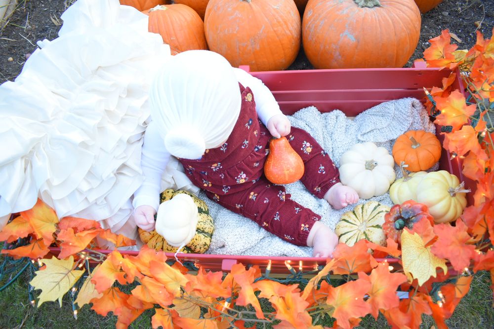 Orange pumpkins and autumn leaves arranged with white fabric in a rustic display.