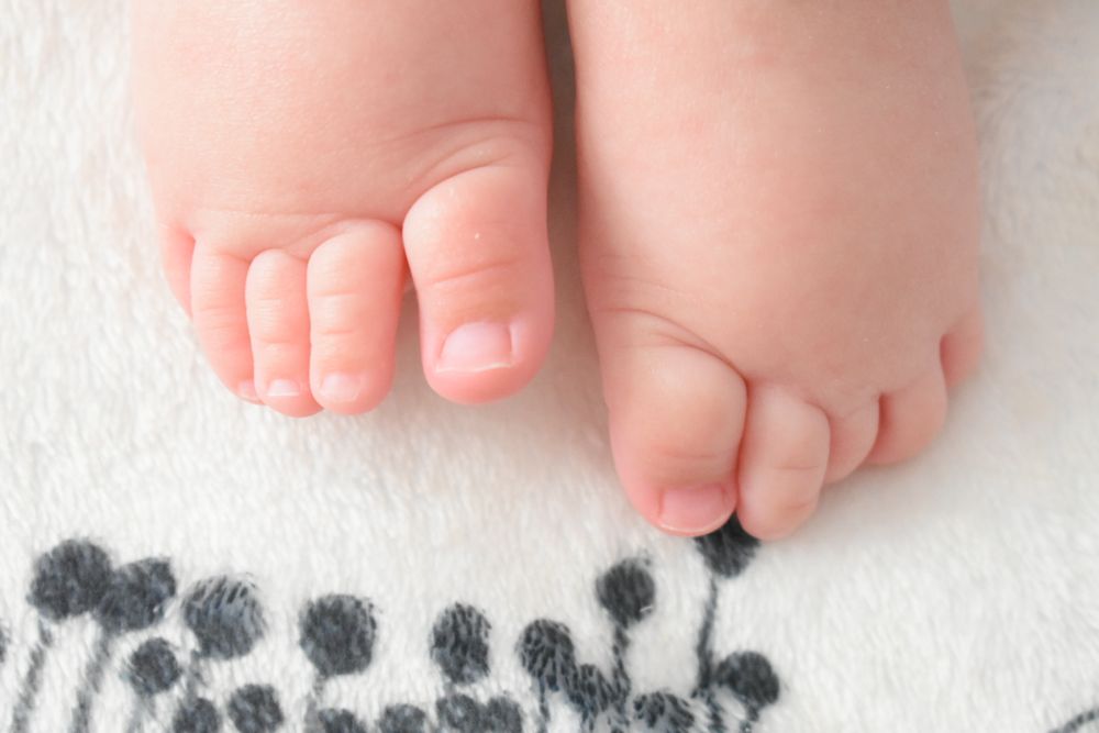 Tiny baby feet resting on a white blanket with decorative gray patterns.
