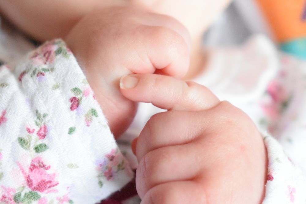 Close-up of tiny baby fingers grasping floral patterned fabric.