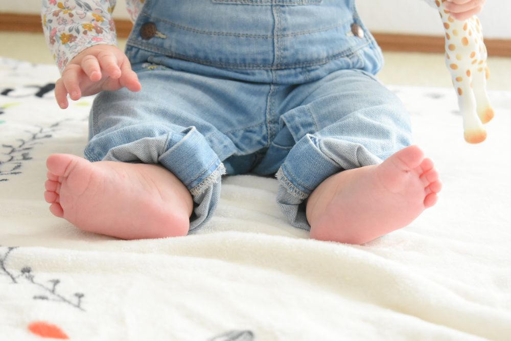 Small feet in rolled-up denim jeans sitting on a patterned blanket.