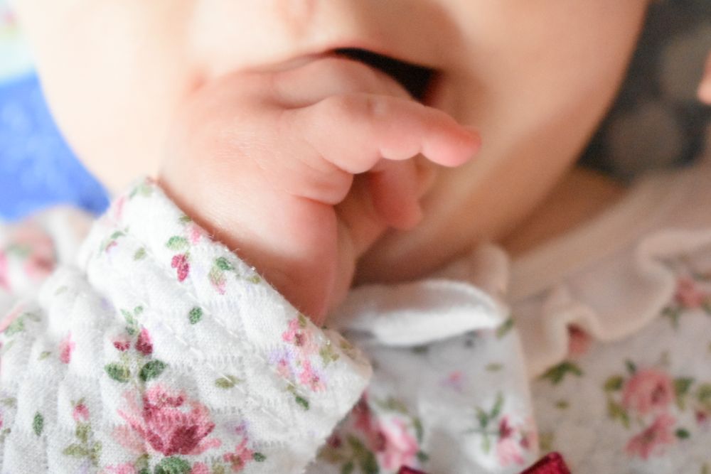 Delicate close-up of baby hand against floral print fabric.