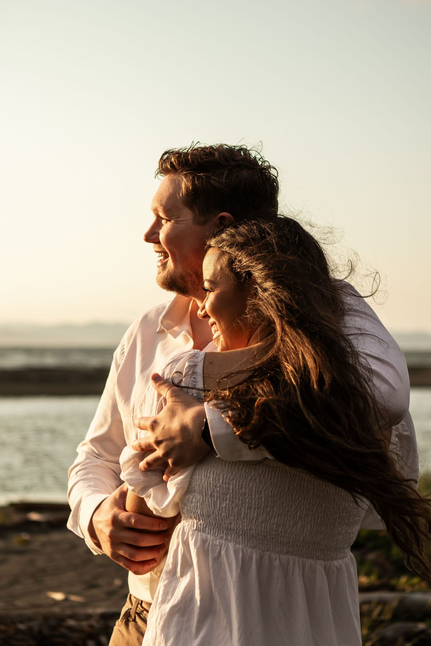 Couple embracing on beach during golden hour with sunlight streaming through.