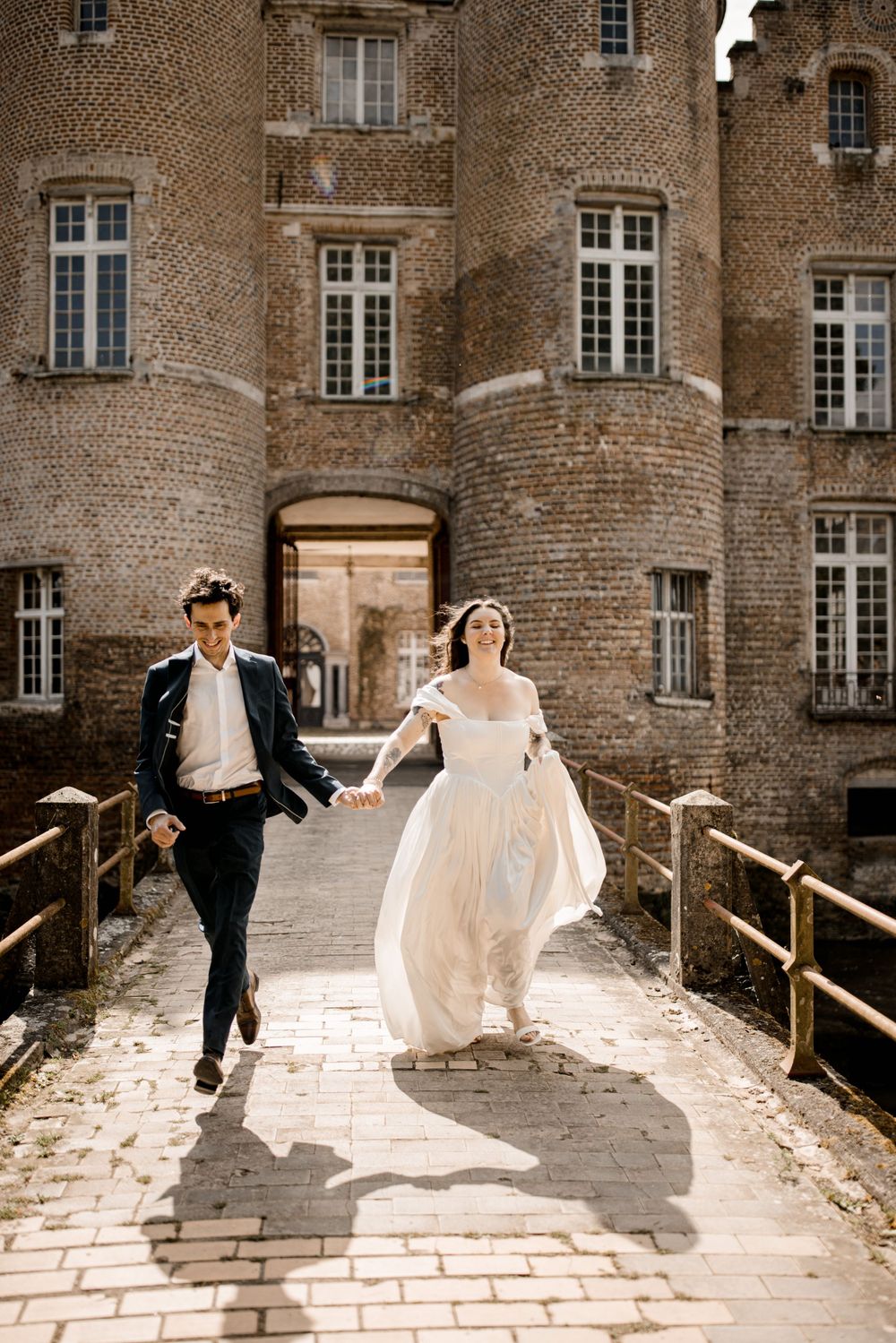 Les jeunes mariés courent main dans la main à travers l'entrée du pont du grand château en briques.