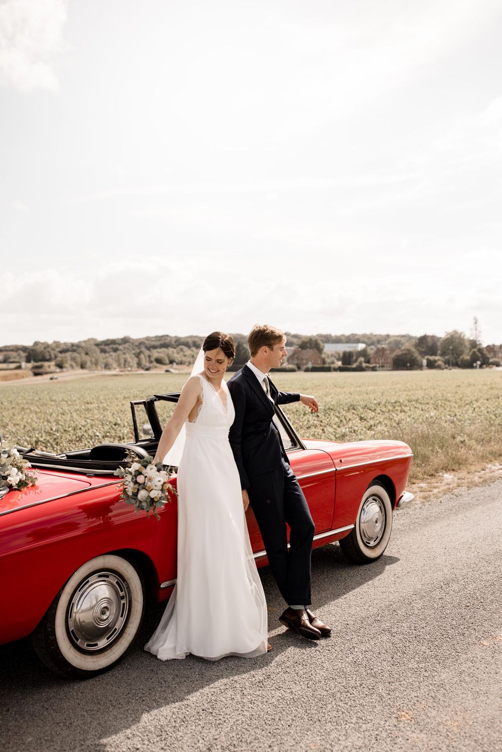 Une voiture vintage rouge classique sert de toile de fond pour une séance photo de mariage.