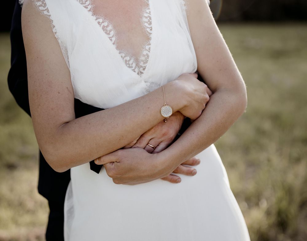 Robe de mariée blanche élégante avec détails en dentelle présentée en gros plan alors que le couple s'embrasse dehors.