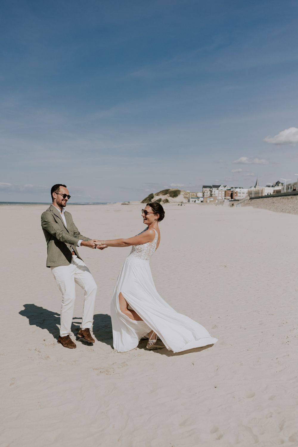 Couple joueur dansant sur une plage de sable avec des maisons en bord de mer en arrière-plan.