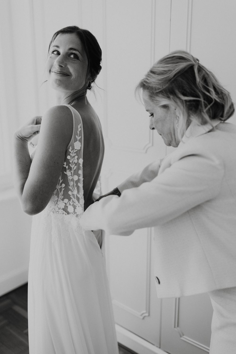 Photo en noir et blanc d'une mariée faisant ajuster sa robe pendant les préparatifs du mariage.