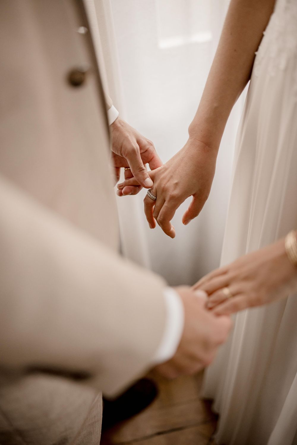 Gros plan de mains se touchant devant un rideau blanc lors d'un moment de mariage intime.
