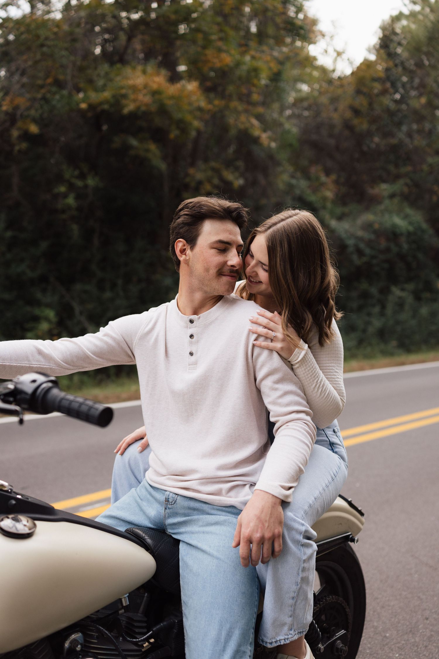 A couple sits together on a motorcycle on a tree-lined road during autumn. Wilmington photographer.