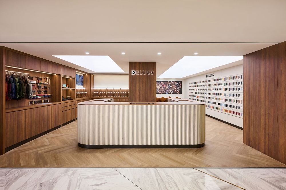 Elegant luxury retail store interior with walnut wood reception desk, herringbone marble floors, and illuminated display shelves.