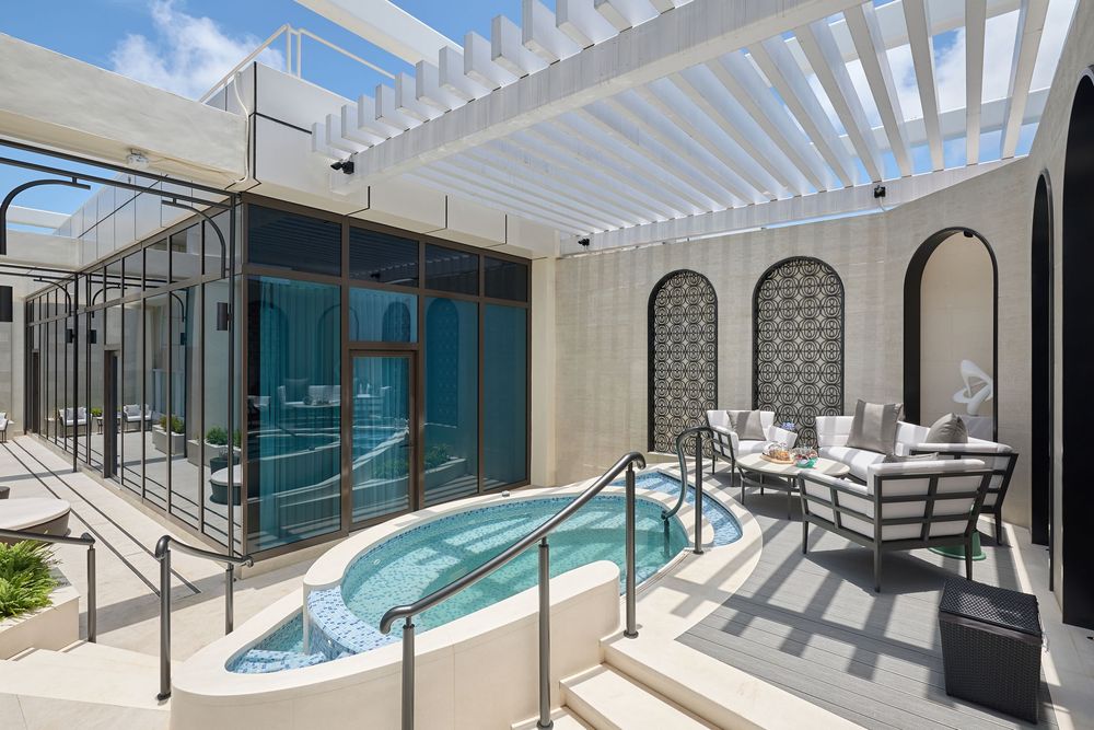 Luxury outdoor spa with a small pool, pergola, arched walls, and elegant patio seating area.
