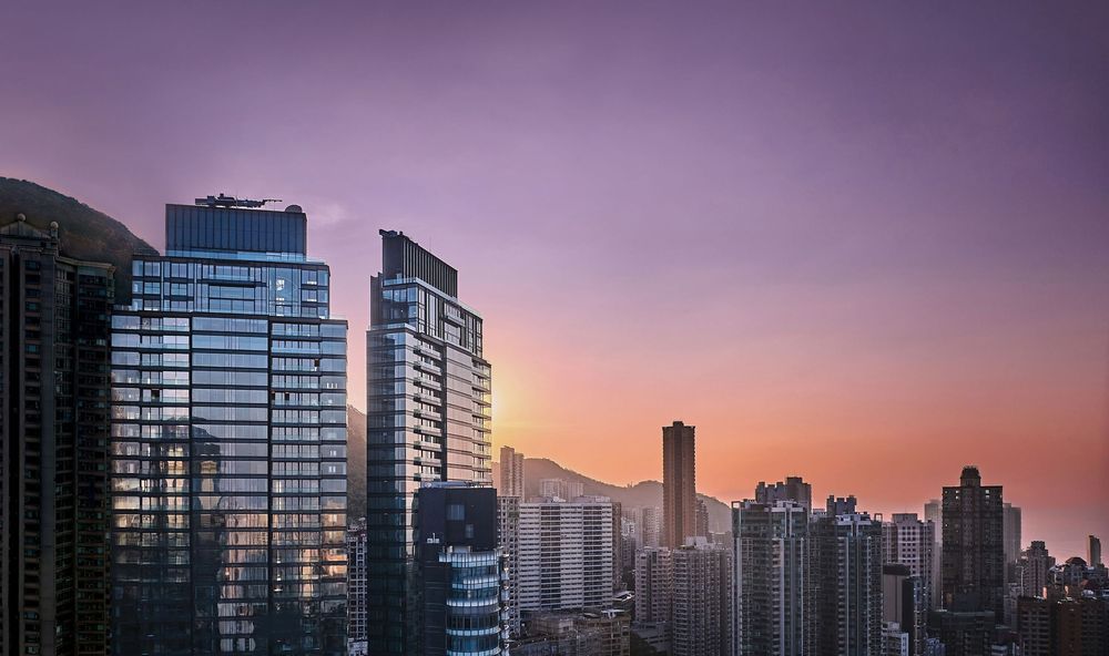 Stunning urban skyline at sunset with modern glass skyscrapers glowing in purple and orange hues over a dense cityscape.