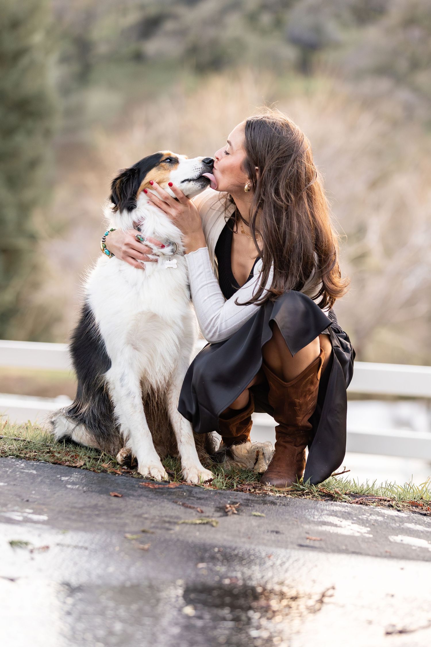 Happy Australian Shepherd dog licking young woman's face while she kneels outdoors.