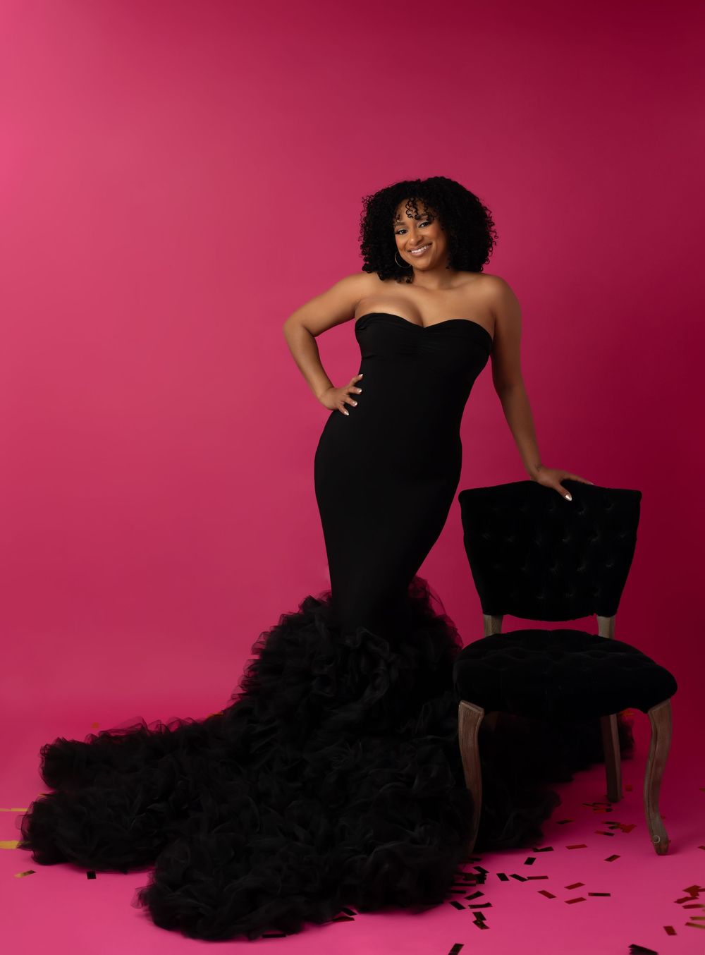 A model in a dramatic black tulle gown poses gracefully against a vibrant pink backdrop in a fashion photoshoot series.