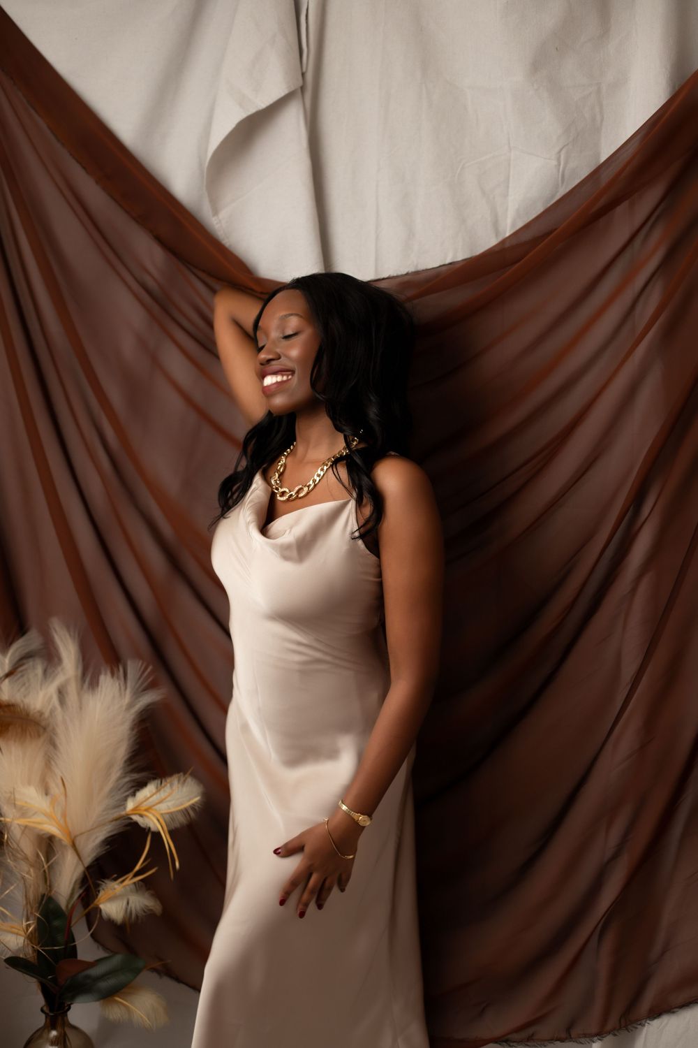 A women looking to be a model in a beige dress poses dramatically against a brown backdrop in a photo series.