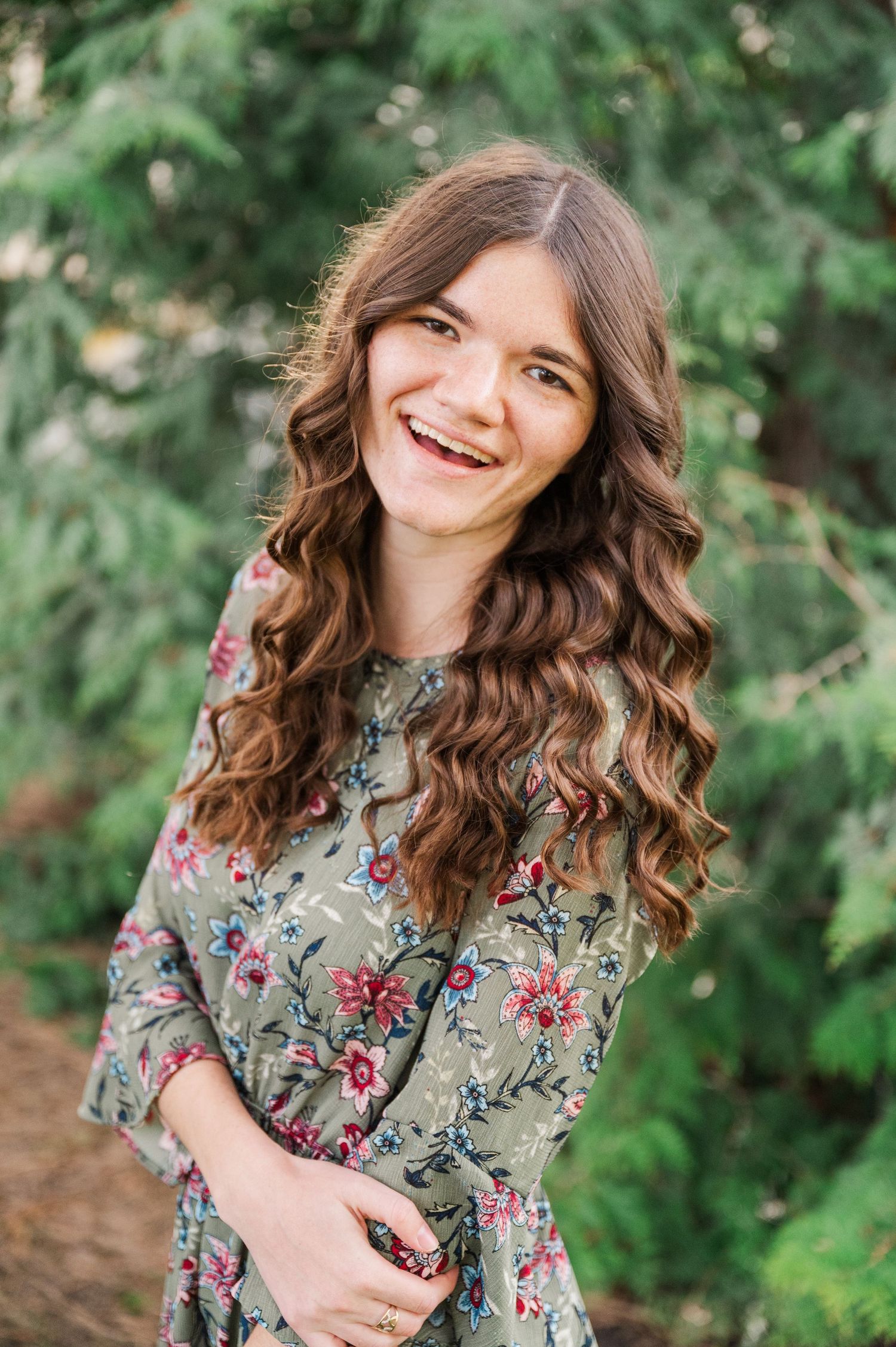 Joyful portrait in floral dress against green foliage background.