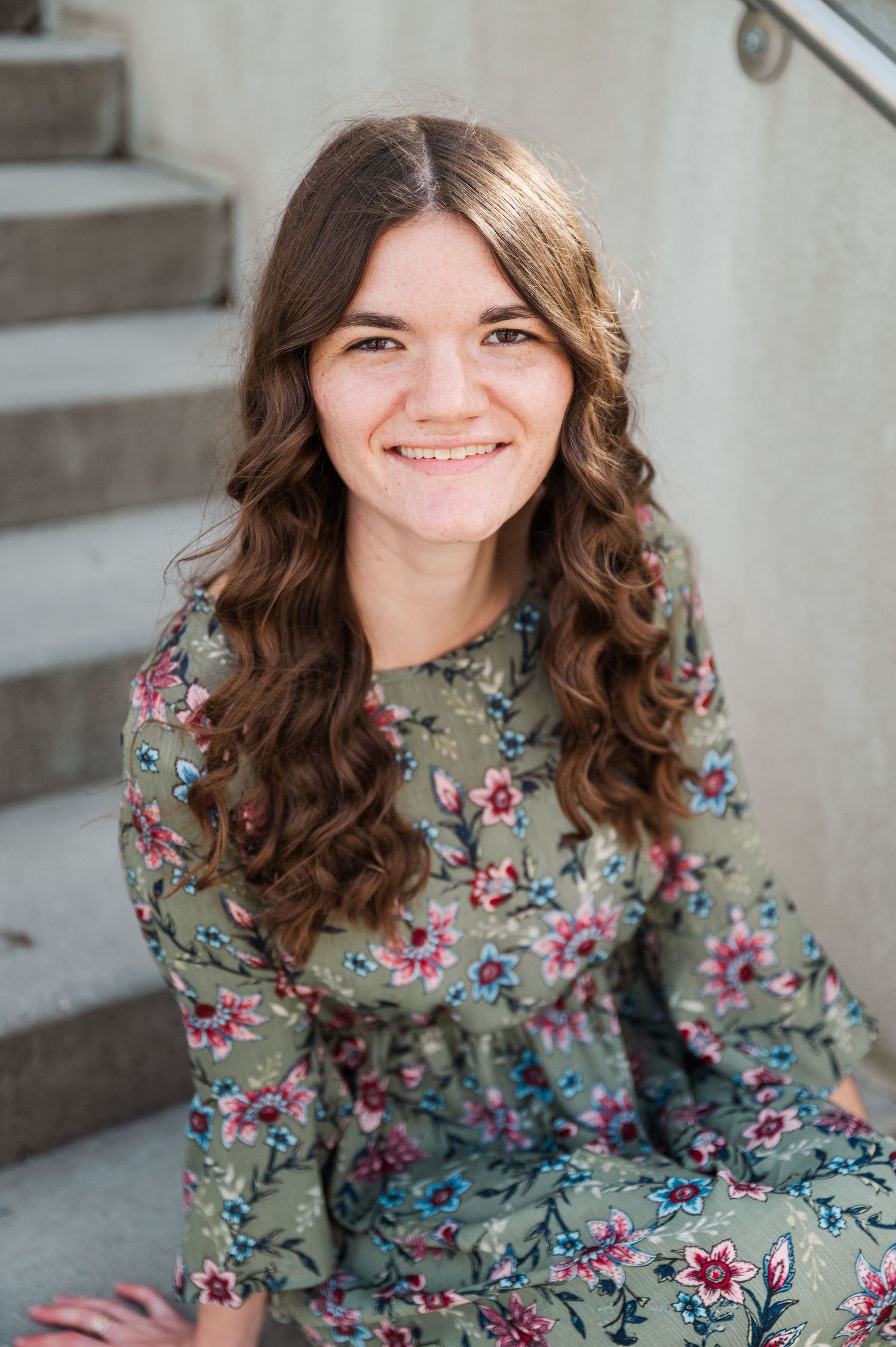 Portrait on concrete steps wearing floral print dress with flowing hair.