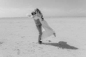 A couple embraces in a romantic black and white moment on an empty beach, creating a dramatic shadow on the sand.