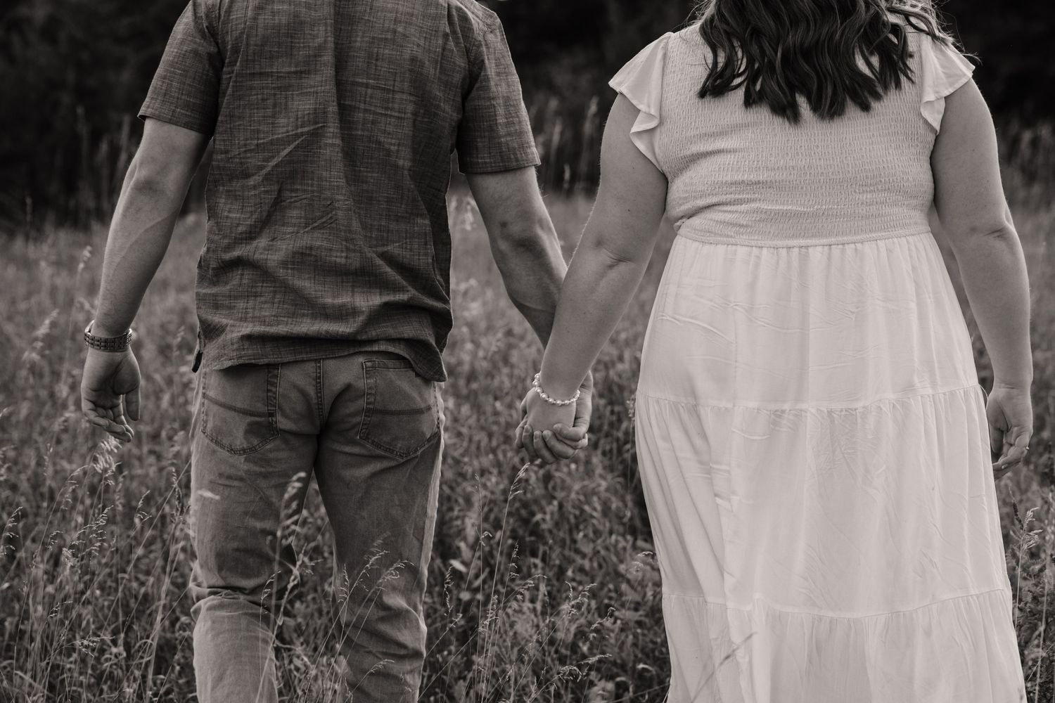 Black and white image of couple holding hands in tall grass field.
