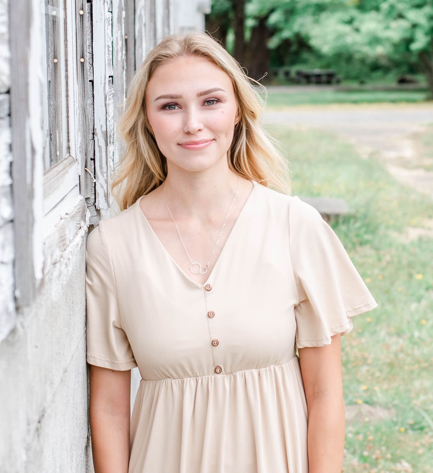 Portrait in cream colored dress against rustic white columns and green foliage.