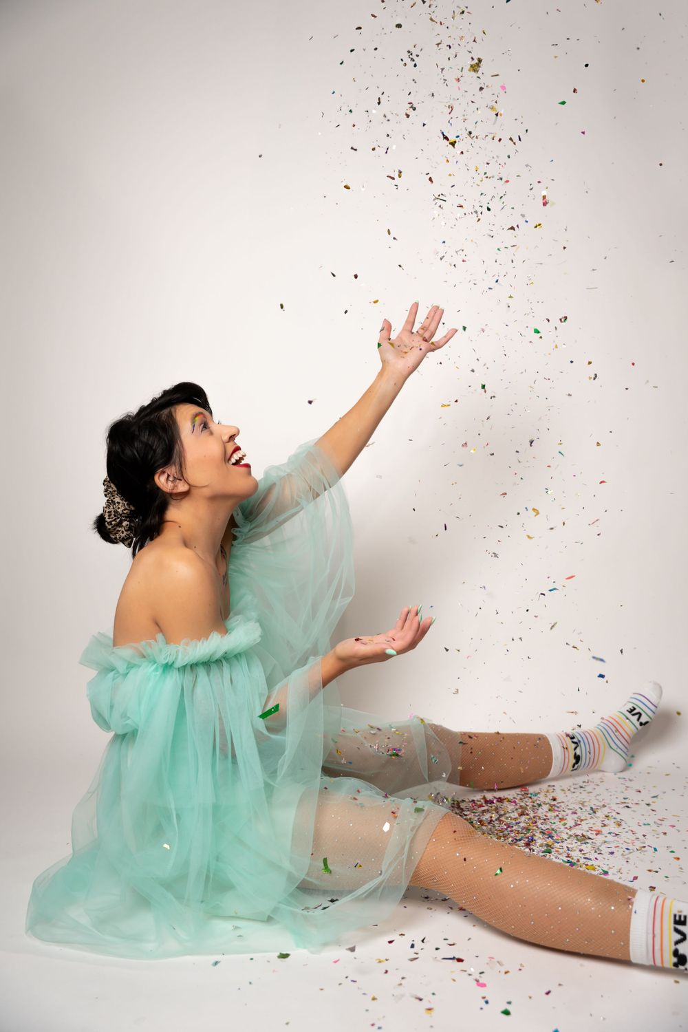 Dynamic poses in mint green tulle dress while confetti falls in studio setting.